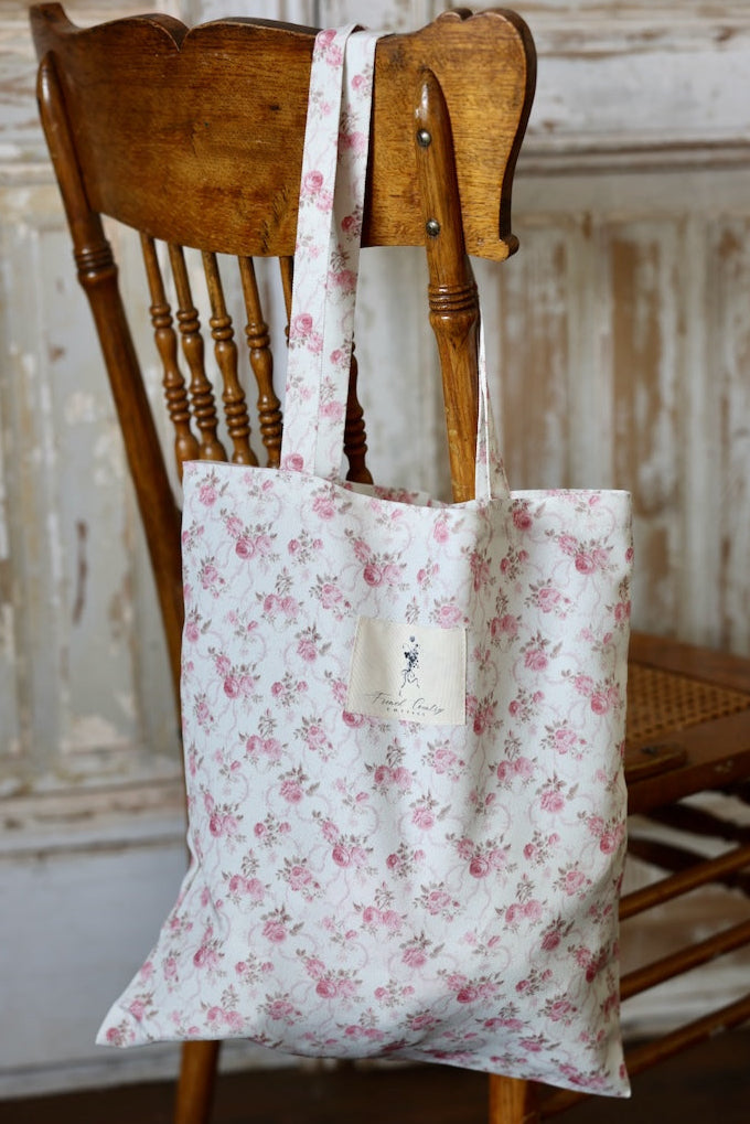 Floral-patterned tote bag hanging on a wooden chair against a rustic wall.